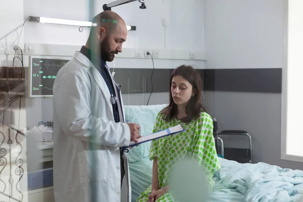 Patienten diskuterer med lægen, mens du sidder på sengen under sygdomsuddrivelsen - Stock-foto