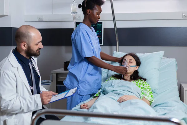 Afro americano asisstant mettere oxigen maschera per malato donna mentre sdraiato a letto — Foto Stock