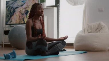 Esnek siyah atlet oturma odasında lotus pozisyonunda dinleniyor.