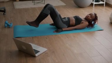 Yoga haritasında oturan ince siyah kadın bisiklet egzersizi yapıyor.