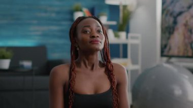 Siyahi kadın antrenör nilüfer pozisyonunda yoga minderinin üzerinde gözleri kapalı oturuyor.