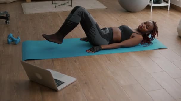 Mujer negra delgada haciendo ejercicio en bicicleta sentado en el mapa de yoga — Vídeos de Stock