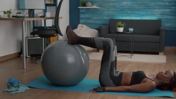 Mujer delgada con piel negra haciendo ejercicio abdominales usando fitball flexionando los músculos abdominales — Vídeos de Stock