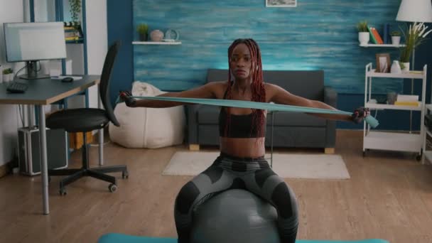 Ajuste mujer negra haciendo ejercicios de yoga usando bandas elásticas en bola suiza — Vídeos de Stock