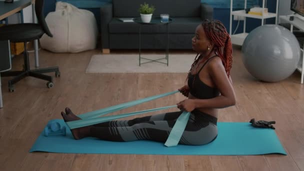 Schlanke Frau mit schwarzer Haut in Sportbekleidung, die mit Fitnessbändern Körpermuskeln trainiert — Stockvideo