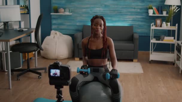 Μαύρη γυναίκα εκπαιδευτής εξάσκηση πρωί γιόγκα άσκηση κάθεται σε swiss μπάλα γυμναστικής — Αρχείο Βίντεο