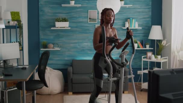 Велосипедистка з чорною шкірою в спортивному одязі тренує м'яз тіла за допомогою еліптичного — стокове відео