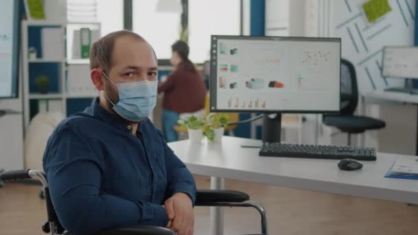 Medewerker met beschermmasker zittend op rolstoel voor de camera — Stockvideo