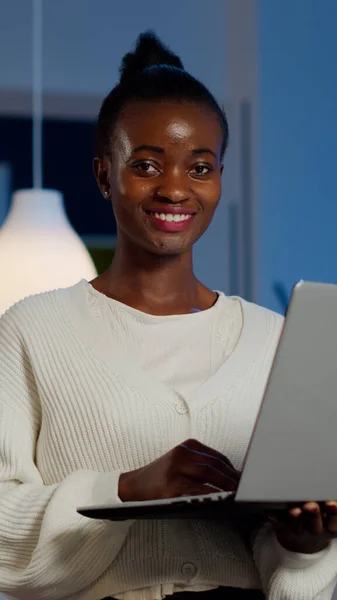 Afrikaanse freelancer kijken naar camera glimlachen houden laptop staan in de buurt van bureau — Stockfoto