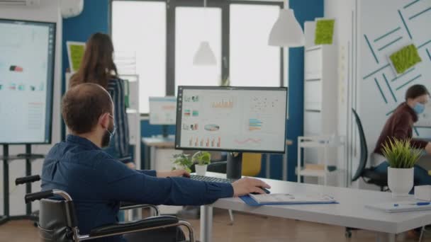 Invalid worker in wheelchair talking with colleague typing on computer — Stock Video