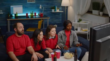 Çok uluslu arkadaşlar kanepede oturmuş futbol izliyorlar.