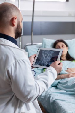 Uzman doktor hasta kadını gözlemliyor. Tablet bilgisayar kullanarak kemik radyografisini açıklıyor.