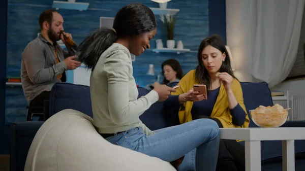 Smíšené rasy přátelé sedí na pohovce držení mobilní v rukou procházení na internetu — Stock fotografie