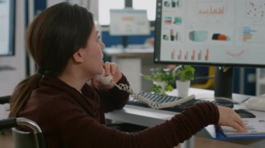 Felç olmuş bir finans uzmanı tekerlekli sandalyede hareketsiz oturarak telefonda konuşuyor.