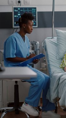 Afro-Amerikalı hemşire hasta kadınla hastalık belirtilerini tartışıyor.