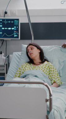 Koyu tenli hemşire hastanın hastane koğuşunda rahat oturmasına yardım ediyor.