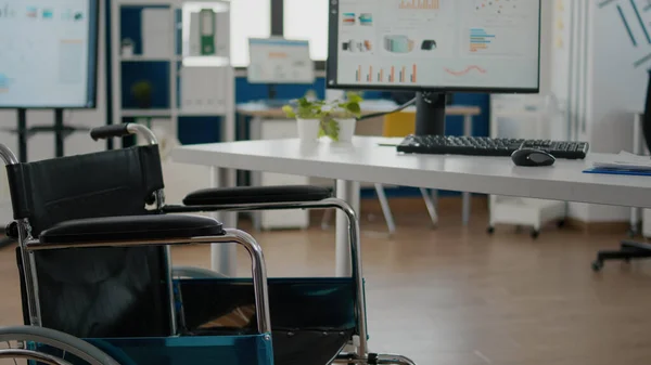 Cadeira de rodas estacionada em sala de escritório vazia perto da mesa na empresa start-up — Fotografia de Stock