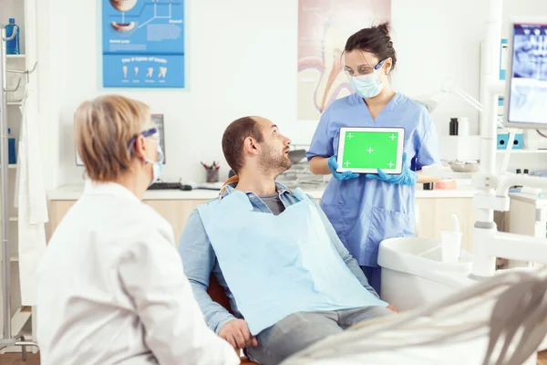 Больной пациент смотрит на сенсорный экран, разговаривая со старшим врачом стоматологом — стоковое фото