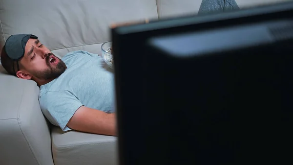 Homem com máscara de sono nos olhos deitado no sofá enquanto assiste filme de entretenimento — Fotografia de Stock
