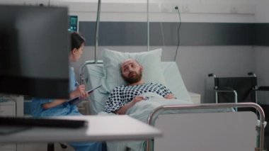 Hasta adam yatakta oksijen tüpüyle oturuyor. Hastalık belirtilerini hemşireye açıklıyor.