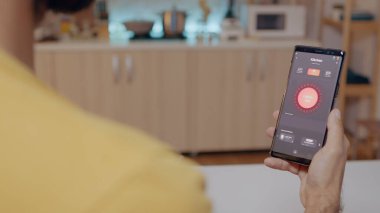 Otomasyon ışığı sistemi olan evde oturan adam akıllı telefon tutuyor.