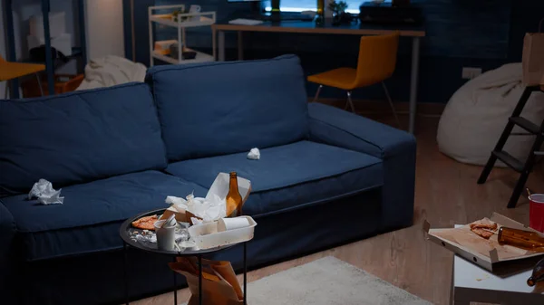 Sobras de pizza botellas de cerveza vacías y servilletas en la mesa en la sala de estar desordenado —  Fotos de Stock