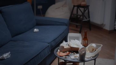 Pizza artıkları, boş bira şişeleri ve sefalet masasında ve yerde peçeteler.