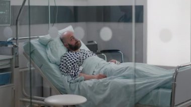 Hasta adam yatakta dinleniyor, nazal oygen tüp takıyor. Hastalık muayenesi için doktor bekliyor.