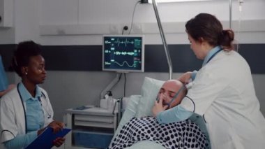 Kadın doktor oksijen maskesi takarken hasta adam yatakta dinleniyor.