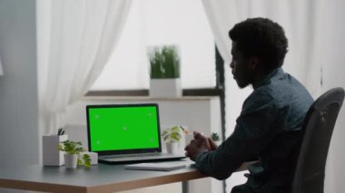 Afrikalı Amerikalı adam yeşil ekranlı bir laptop kullanıyor.