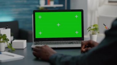 Parlak oturma odasında yeşil ekran laptop kullanan Afro-Amerikan bir adamı kapatın.