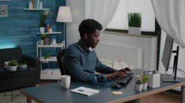 Afrikalı etnik kökenli serbest çalışan biri evden çalışırken kulaklık takıyor.