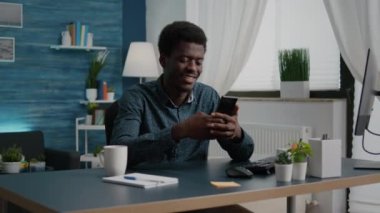Otantik siyah Afrikalı Amerikalı adam akıllı telefon kullanırken gülümsüyor.