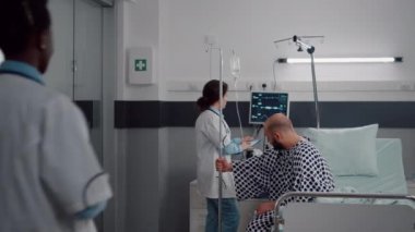 Hekim doktorlar hastanın ayağa kalkmasına yardım ediyor. Damardan damar içi sıvı torbası tutuyorlar.