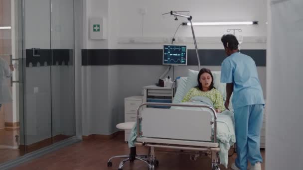 Afro american nurse arrange sick woman bed during medical recovery — Stock Video