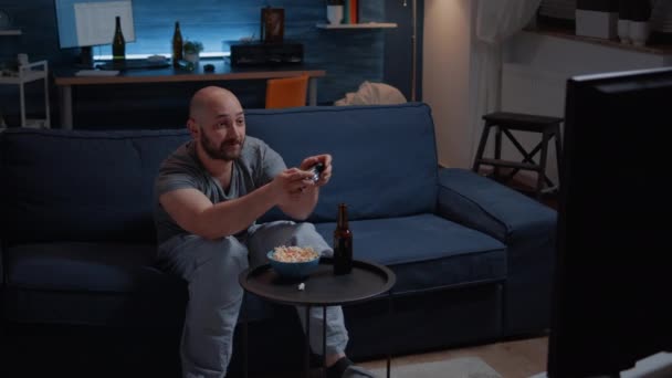 Визначений збуджений чоловік сидить на дивані, граючи у відеоігри — стокове відео