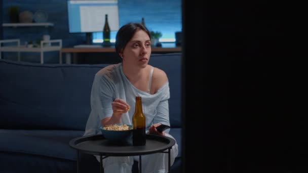 Эмоциональная молодая женщина ест попкорн во время просмотра отвратительного телевизионного фильма — стоковое видео