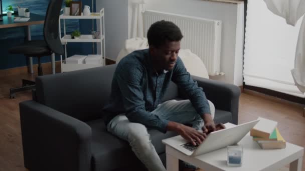 Retrato del hombre negro en la sala de estar escribiendo en el ordenador portátil — Vídeo de stock