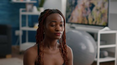 Nilüfer pozisyonunda oturup vücut kaslarını geren ince yapılı zenci kadın antrenör portresi.