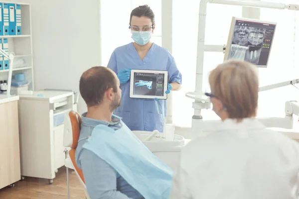 Enfermeira estomatologista apontando na tela digital explicando raio-x do dente para o homem doente — Fotografia de Stock