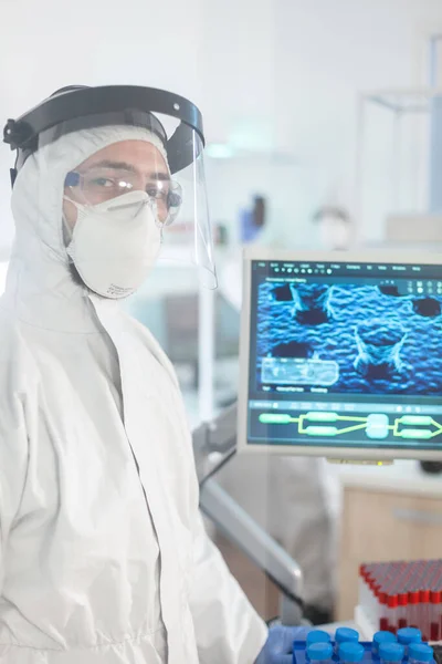 Микробиолог в костюме ppe стоит в лаборатории и смотрит в камеру — стоковое фото