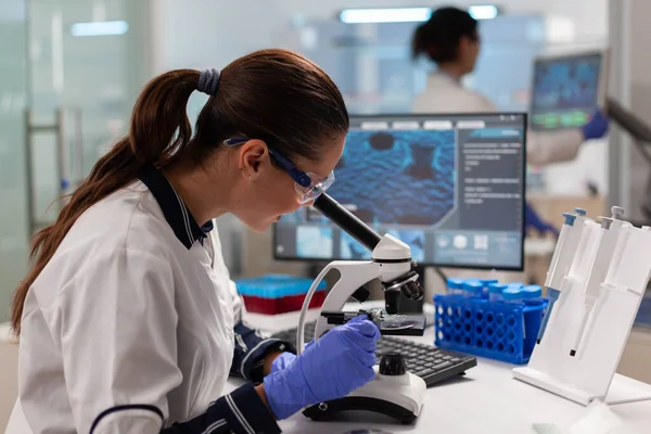 Científico con gafas de protección investigando muestra mirando a través del microscopio —  Fotos de Stock