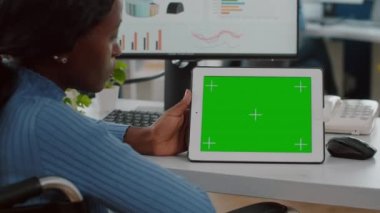 Tekerlekli sandalyedeki özürlü Afrikalı çalışan yeşil ekranlı tablete bakıyor.