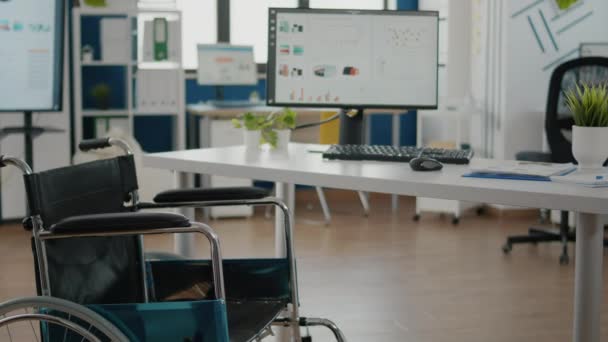 Wózek inwalidzki zaparkowany w pustym pomieszczeniu biurowym przy biurku w firmie start-up — Wideo stockowe