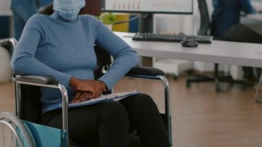 Yüz maskesi takan engelli siyah proje yöneticisi kameraya bakıyor