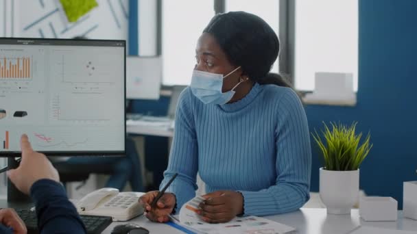 Afrikanischer Mitarbeiter mit Gesichtsmaske erklärt kranken Mitarbeiter Projekt — Stockvideo
