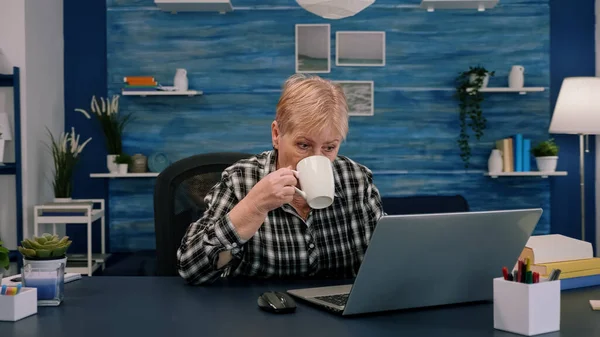 노트북으로 일하면서 커피를 마시고 있는 나이든 여자 — 스톡 사진