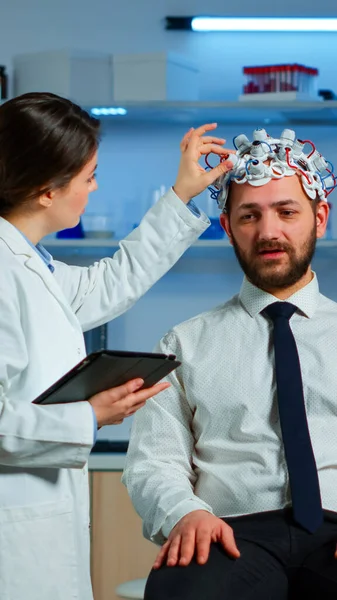 Paciente con auriculares de escaneo de ondas cerebrales discutiendo con investigador neurológico —  Fotos de Stock