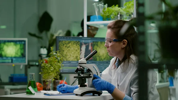Pharmaceutical scientist looking at green leaf sample on microscope — Stock Photo, Image