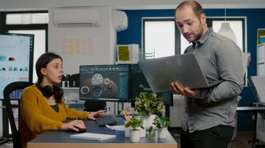 Proje yöneticisi dizüstü bilgisayar tutuyor ve kadın mühendis ile konuşuyor.